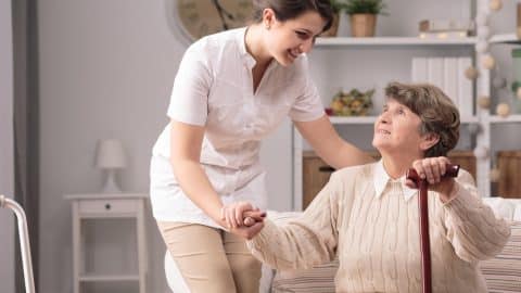 Young Carer Supporting Senior Disabled Woman With Walking Stick